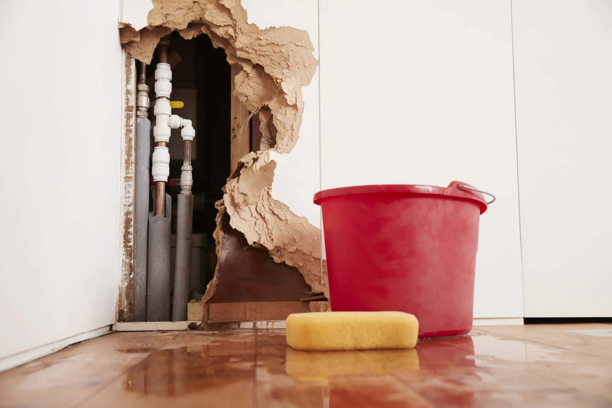 Burst plumbing exposed inside a damaged wall with emergency water collection